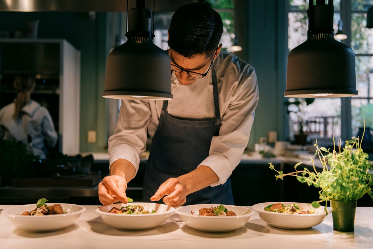 Male chef garnishing food with herb under light at commercial kitchen